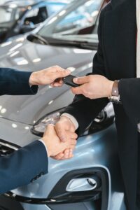 Man receiving key to new car while shaking hands on the deal