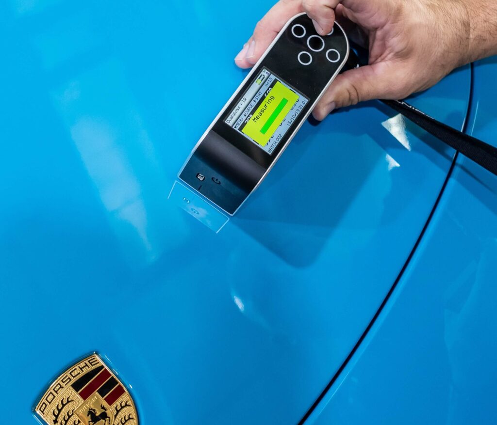 man-holding-device-near-blue-porche-car