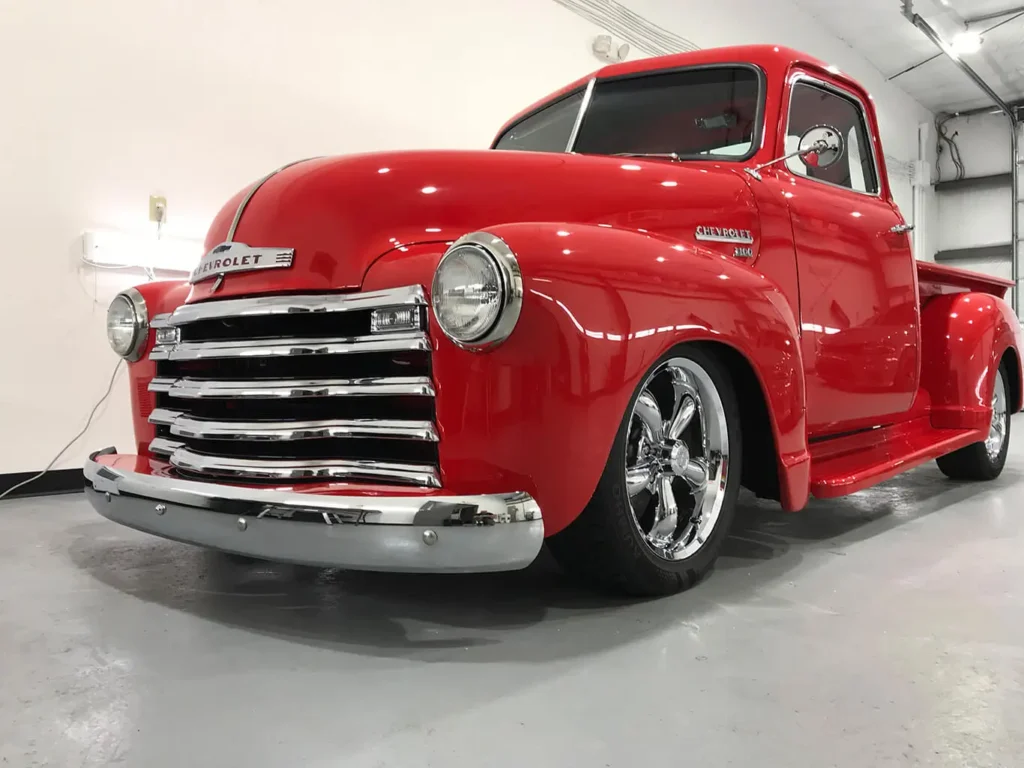 Restored red classic Chevrolet pickup truck with chrome details displayed indoors.