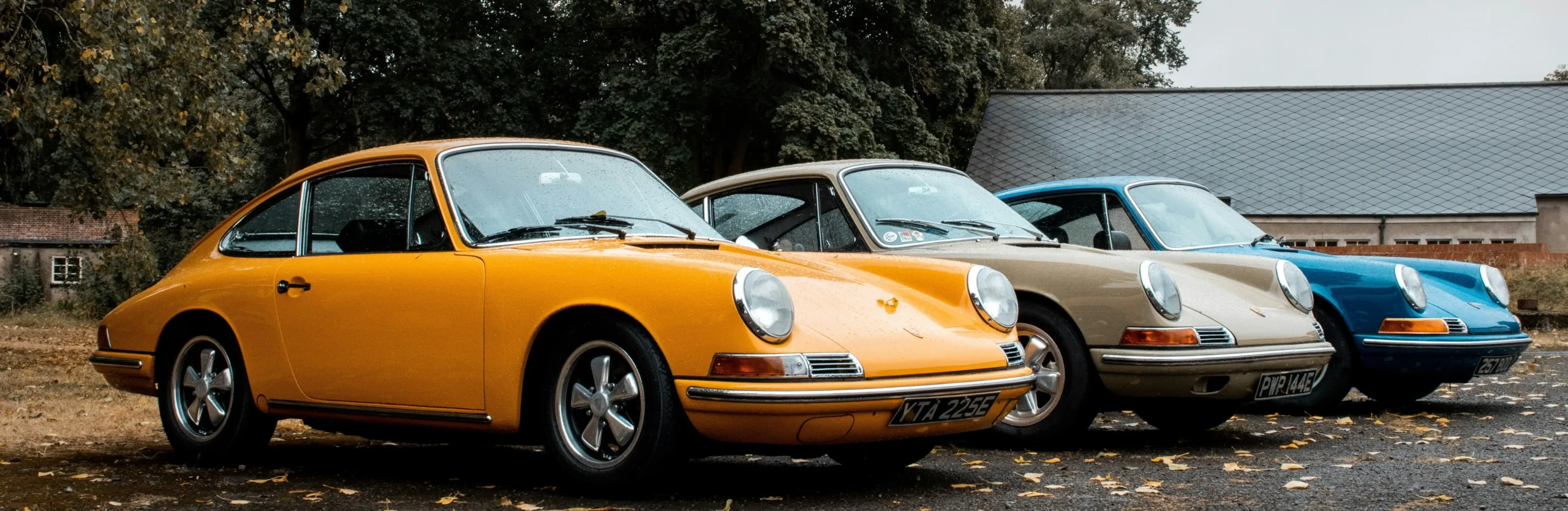 Three classic Porsche 911 sports cars parked side by side in different colors at an outdoor location