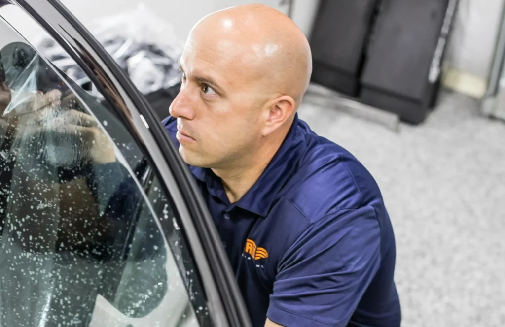 Technician installing window film on a car door inside an automotive workshop.