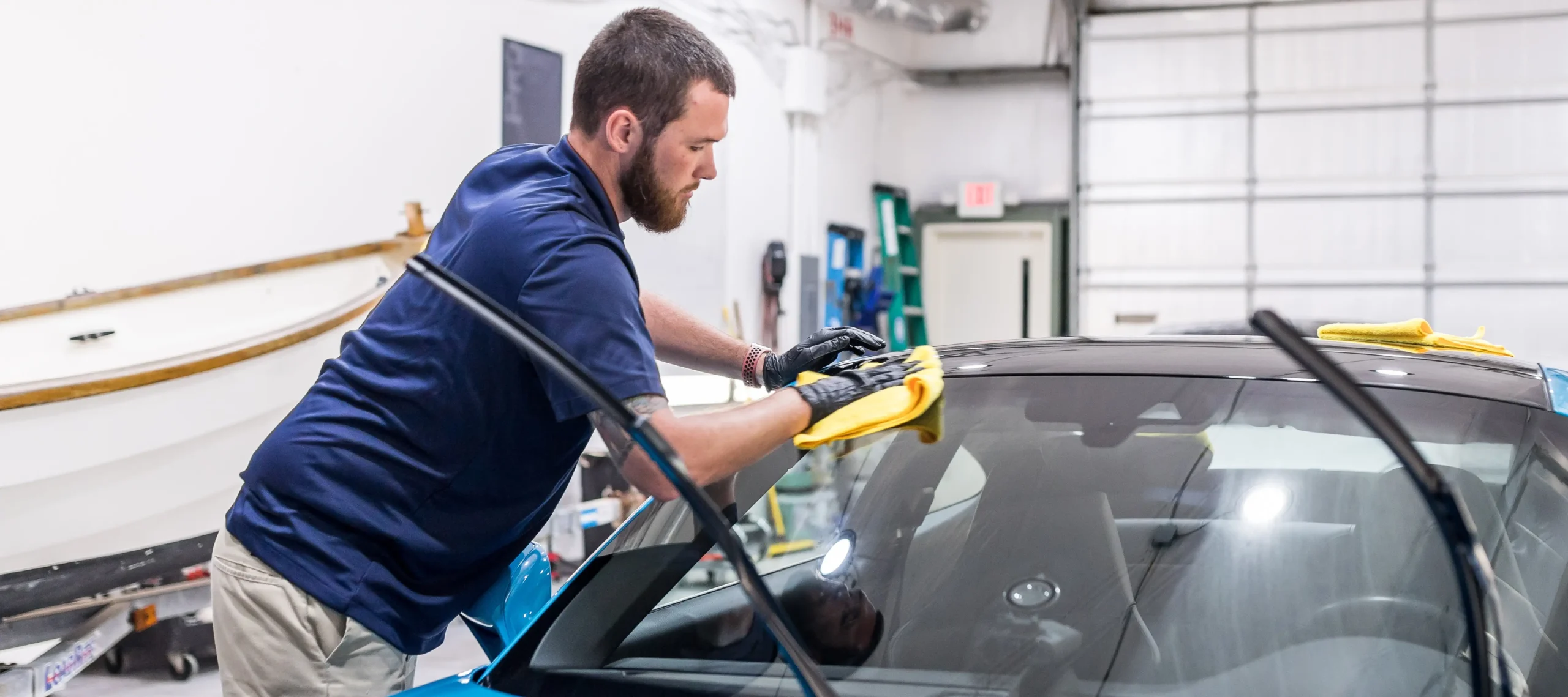 Technician applying window tint film to a car windshield inside an automotive workshop.